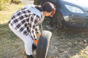 Young Asian woman changing a car tire in the countryside on a sunny day