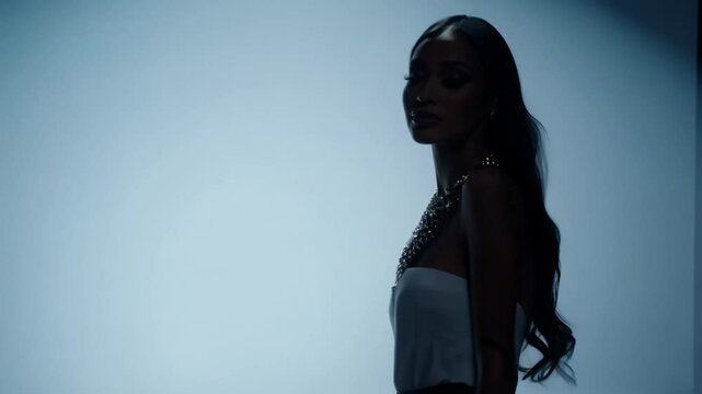 Camera zooms out on a model with long, straight hair and statement necklace in a studio setting