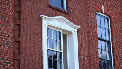 Naklejka premium Elegant Red Brick Building with White Trimmed Windows, Perfect for Architectural Photography or Home Decor Inspiration
