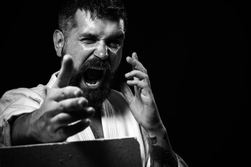 Portrait of screaming handsome karate man breaking concrete brick. Angry karate fighter smashes...