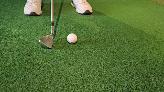 A golfer prepares to hit a shot with a wedge on a putting green in an indoor facility during a practice session