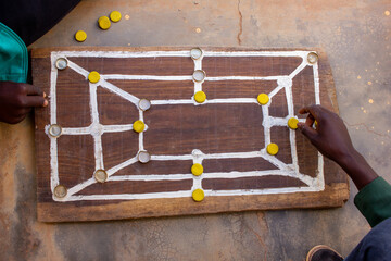 Traditonal african strategy board game know as morabaraba, equivalent to twelve men's morris, a variant of Nine men's morris, being played on a wooden board using recycled bottle caps