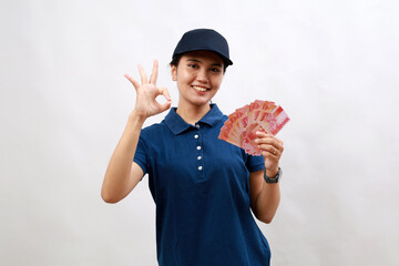 Young hispanic woman courier wearing delivery uniform and cap holding indonesia rupiah doing ok sign with fingers, smiling friendly gesturing excellent symbol