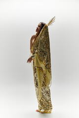 An enchanting figure adorned in a shiny golden dress captures the essence of beauty and grace in a studio.