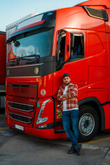 Smiling trucker posing for photo while leaned on big red truck with crossed hands.