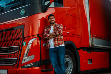 Smiling trucker posing for photo while leaned on big red truck with crossed hands.