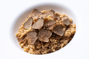 Black truffle risotto recipe. Autumn creamy consistency risotto in stylish white dish on the white background. Autumn gourmet cuisine of Piedmont, Northern Italy, France, Spain, close up