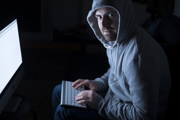 Portrait of hacker in the sitting in front of computer with glow