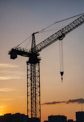 Silhouette of a tall building crane against the sunset, representing construction and progress