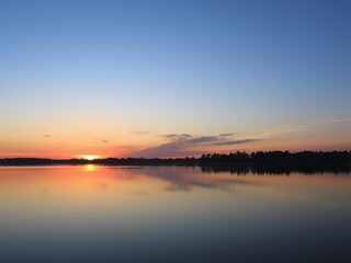 Vibrant sunrise over a calm lake with silhouetted trees in the foreground, serene, nature