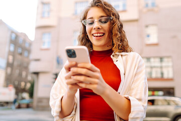 Woman using smartphone while standing outdoors at sunset. Technology, connection, blogging, modern lifestyle concept
