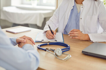 A woman doctor in a clinic takes notes after examining a patient, close-up. There is a stethoscope on the table. Concept of medic appointment, referral for tests, disease treatment strategy