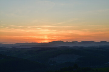The orange sunset and its rays dazzle the green forests and meadows