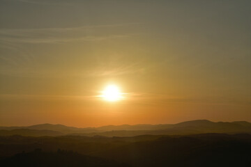 The orange sunset and its rays dazzle the green forests and meadows
