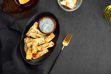 Healthy zucchini fries with yogurt and herbs sauce on dark background with copy space