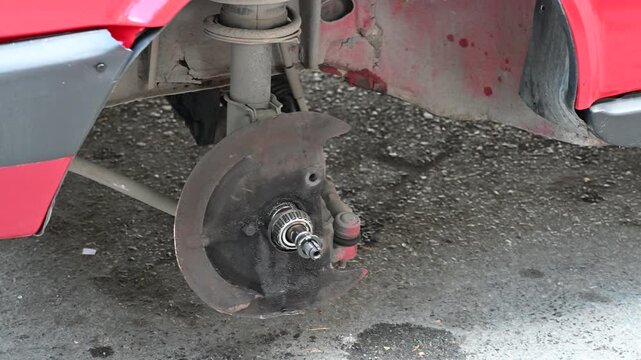 Car with Wheel Removed Exposing Brake and Suspension. Close-up of a car missing a wheel, showing the exposed brake rotor, suspension, and wheel well in a repair or maintenance setting.

