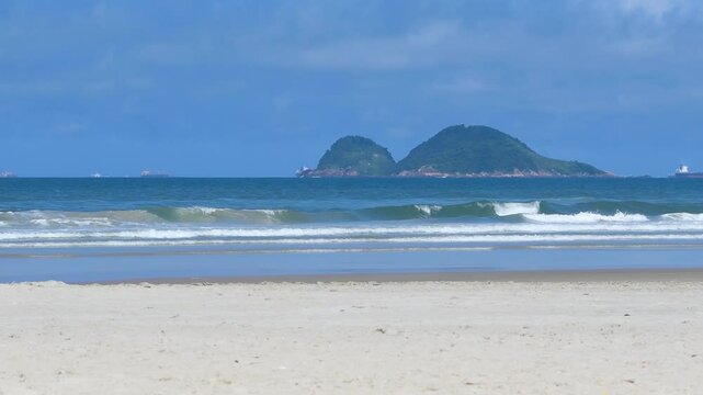 Morning at Enseada Beach on a beautiful day, view of the beach sand, the sea, and the Farol da Moela island on background. Guaruja - SP, Brazil.