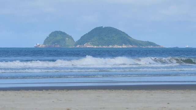 Morning at Enseada Beach on a beautiful day, view of the beach sand, the sea, and the Farol da Moela island on background. Guaruja - SP, Brazil.
