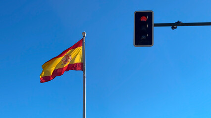 Spanish flag flies near a red traffic light in a clear blue sky. City life Spain