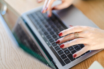 Close-up of a woman's hands with red nails typing on a laptop keyboard