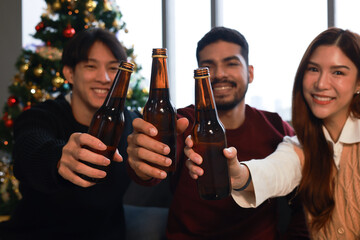 Happy group of friends cheering  and drinking beer  and making a toast during  Christmas celebration in the living room at home 
