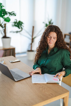 Thoughtful young woman holding studying, with a laptop and notebook in front of her