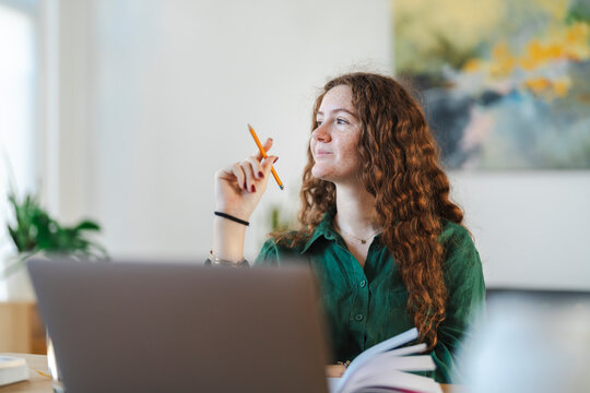 Thoughtful young woman holding studying, with a laptop and notebook in front of her