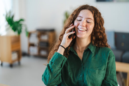 A cheerful young woman smiling while on a phone call in a cozy home office setting