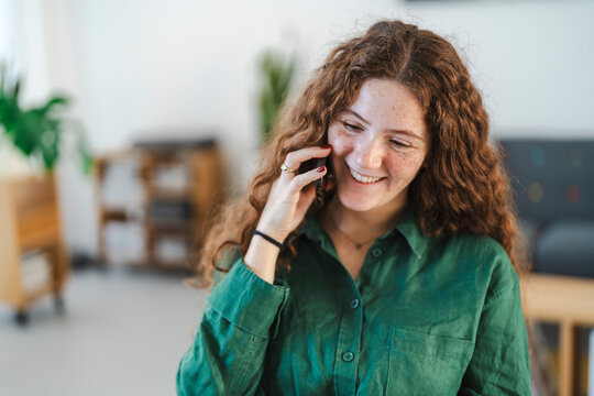 A cheerful young woman smiling while on a phone call in a cozy home office setting