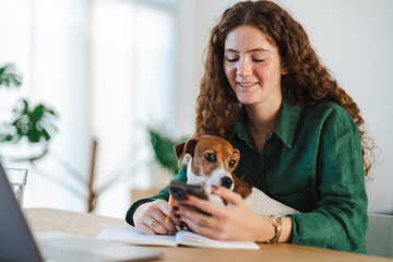 Young woman working at her desk with her dog on her lap in a casual workspace