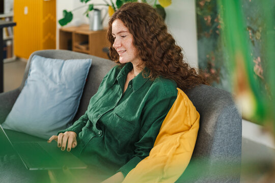 Woman lounging on a couch with a laptop, engaged in remote work or browsing in a relaxed and comfortable home setting