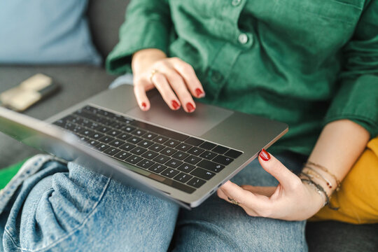 Close-up of a woman's hands with red nails typing on a laptop keyboard