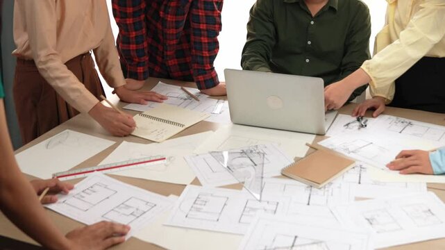 Architect and safety engineer discussion about building blueprint displaying on laptop on table with architectural document and wooden block scatter around at modern office. Closeup. Delineation.