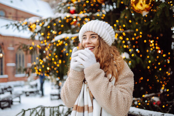 Pretty woman drinks a hot drink at a Christmas market decorated with festive lights. Spending winter holidays.