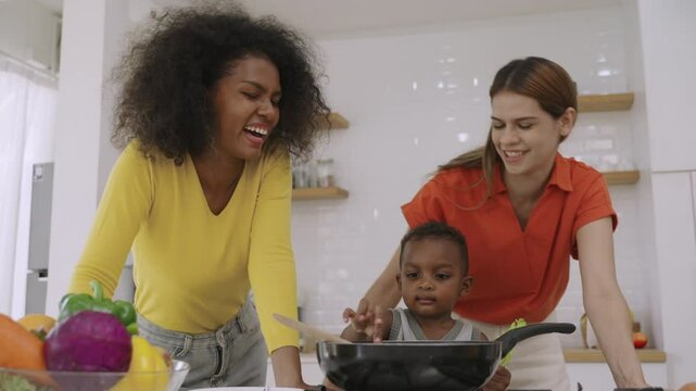 Family of happy interracial lesbian couple and black cute son spend their leisure cooking breakfast together with love and affection in the kitchen room at home. Female homosexual LGBTQ pride concept.