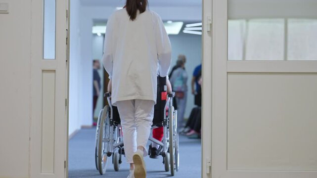 Healthcare worker pushing a wheelchair with male patient down a hospital corridor. Concept of assistance, healthcare support, medical care in a clinical setting, recovery, rehabilitation, helping