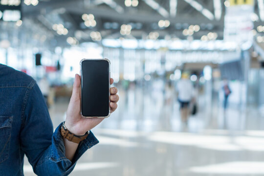Asian man passenger wearing protective face mask showing e-ticket to flight. Touris man showing boarding pass on mobile phone. Young male showing smartphone at airport.
