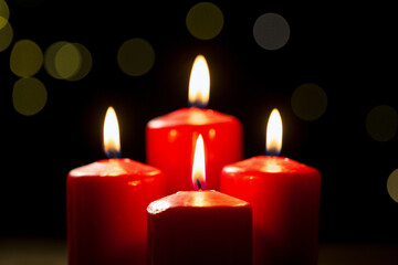Four burning red candles on a festive black background with golden decoration, close-up shot. Advent, Christmas, holiday, and tradition concepts.