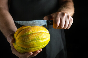 In a dimly lit kitchen, a skilled chef holds a bright melon, poised with a sharp knife, ready to...