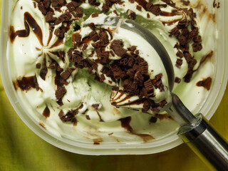 Closeup overhead shot of a spoon tool taking a scoop of melting ice cream with chocolate swirls from a tub. Use as either a horizontal or vertical orientation.