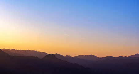 Serene mountain landscape at sunset with layered silhouettes of mountain