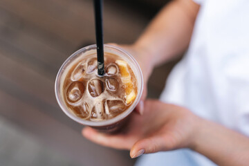 Closeup top view of female hand holding ice beverage drink, iced coffee standing on city street. Woman drinking cold bubble tea through straw, enjoying free time in travel. - Powered by Adobe