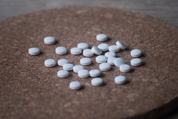 A pile of round white pills on a wooden background. The pills are scattered on the surface.