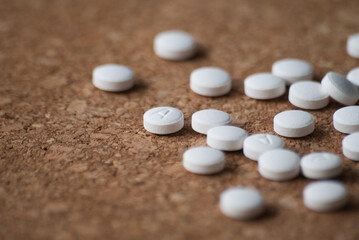 A pile of round white pills on a wooden background. The pills are scattered on the surface.