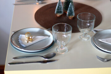 Table set for Christmas meal with plates, glasses, holiday decorations, lit candles and wine. Selective focus.
