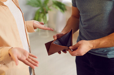 Poor husband showing wife an empty, open wallet in hands, symbolizing financial hardship and...