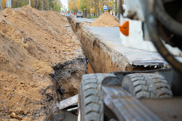 An excavator next to a deep long earthen trench for laying a large diameter water pipe....