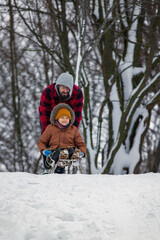 A little boy, a happy smiling child sits on a sled getting ready to slide down a hill in the snow in winter. Childhood concept, lifestyle