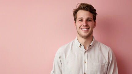 Obraz premium Cheerful Young Man in Casual Attire Against Soft Pink Background for Relaxed Portrait