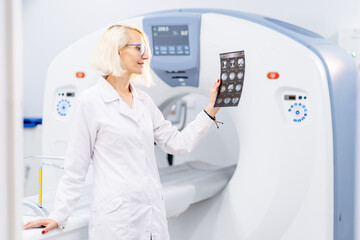 Blond woman stands confidently by MRI machine
